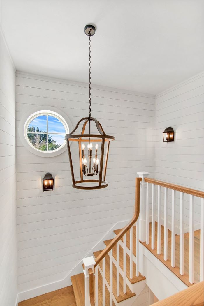 Looking from balcony down the Timeless shiplap wall staircase with farmhouse chandelier and round window 