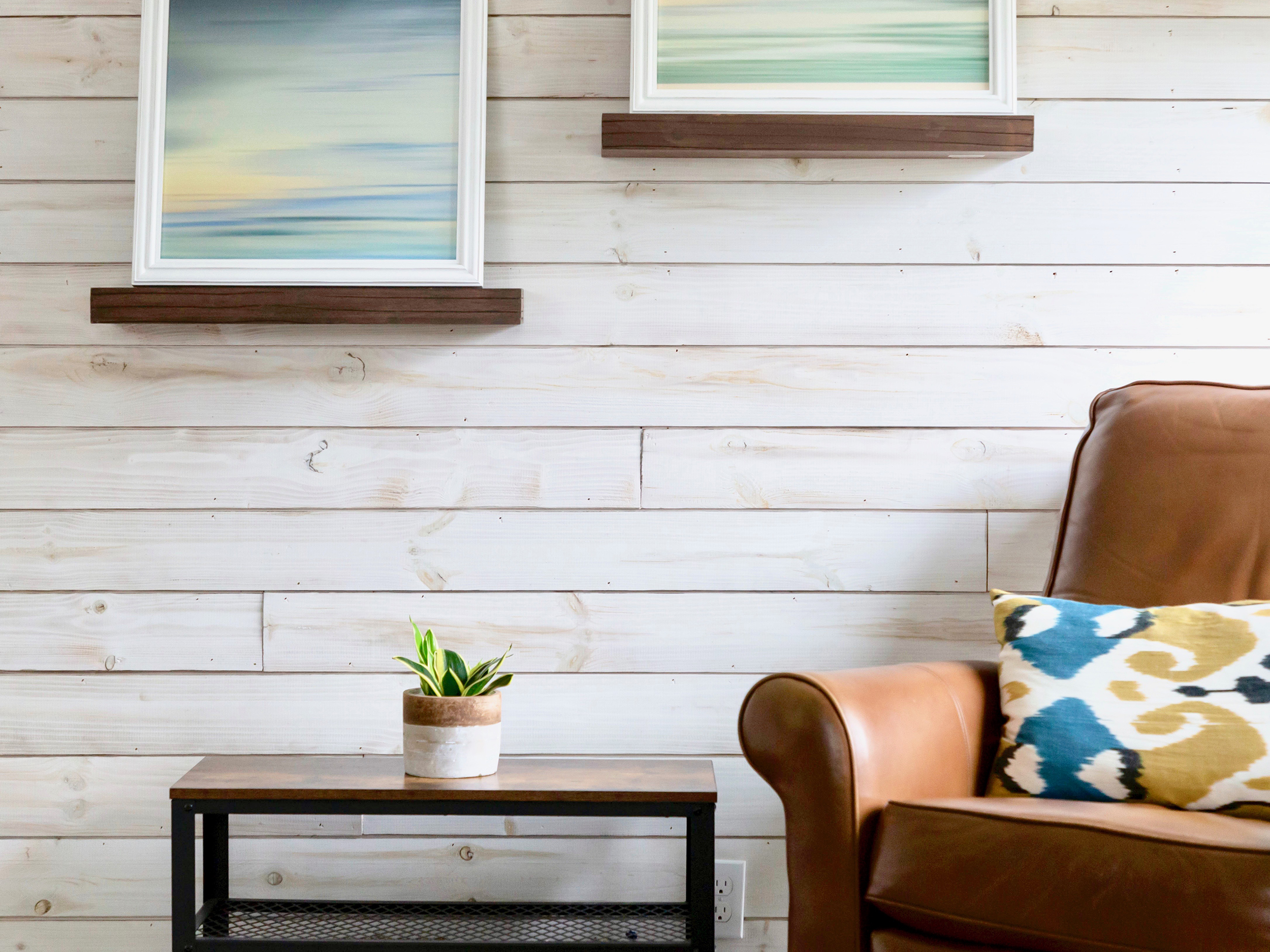 Charred Smoke White shiplap accent wall with cognac leather chair, picture frames, and plant